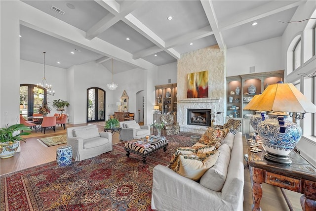 living room with beamed ceiling, wood-type flooring, an inviting chandelier, and a high ceiling