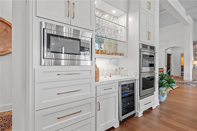 kitchen featuring wine cooler, light wood-type flooring, light stone counters, white cabinetry, and stainless steel appliances