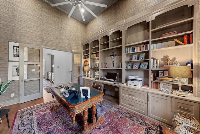 office area with ceiling fan, built in shelves, a towering ceiling, beamed ceiling, and wood-type flooring