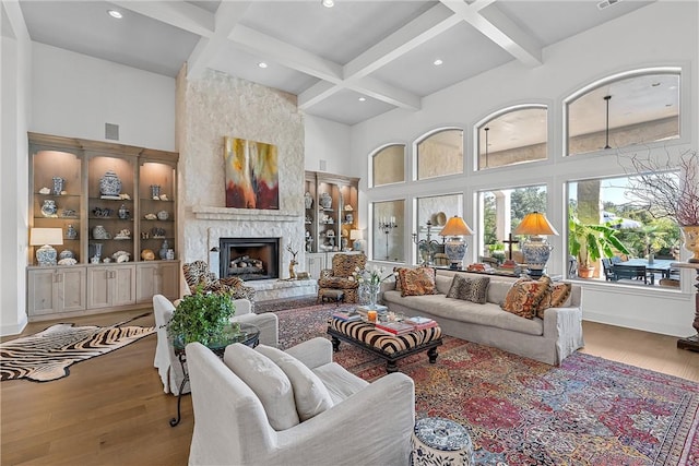 living room with light wood-type flooring, a towering ceiling, coffered ceiling, beam ceiling, and a fireplace