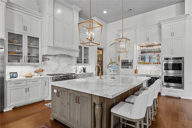 kitchen with appliances with stainless steel finishes, a center island with sink, white cabinetry, and sink