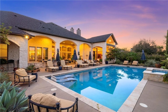 pool at dusk featuring a patio area and an in ground hot tub