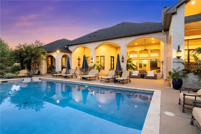 pool at dusk featuring ceiling fan, a patio, and an outdoor living space