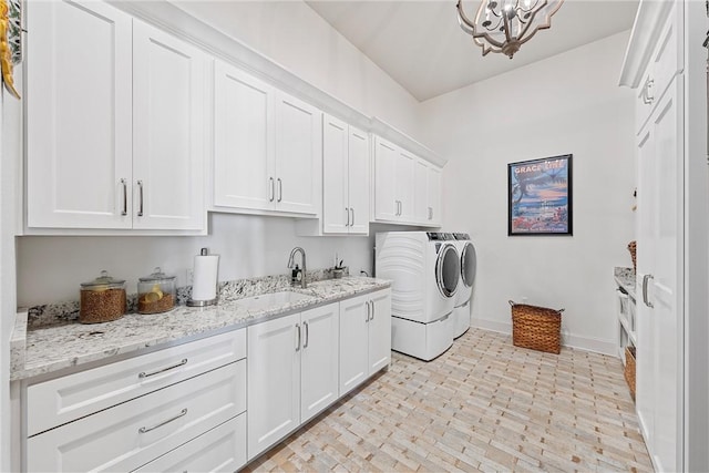 clothes washing area with washer and clothes dryer, a notable chandelier, cabinets, and sink