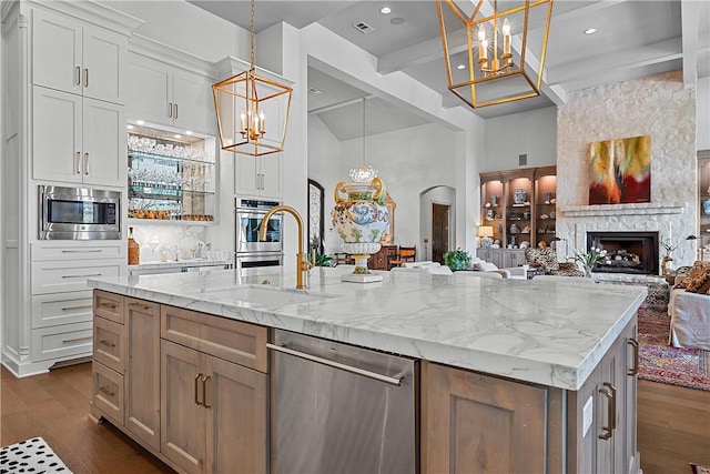 kitchen featuring white cabinetry, stainless steel appliances, a stone fireplace, pendant lighting, and a kitchen island with sink