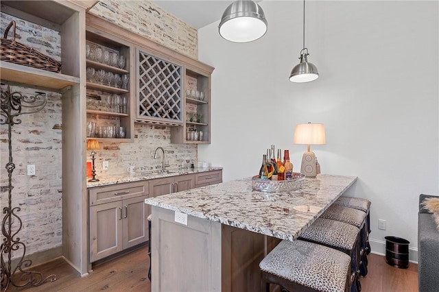 bar with dark hardwood / wood-style flooring, light stone counters, sink, and hanging light fixtures