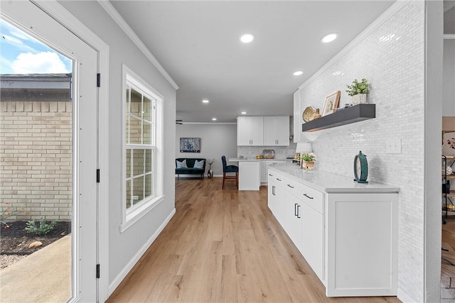 kitchen with white cabinets, decorative backsplash, light wood-type flooring, and crown molding