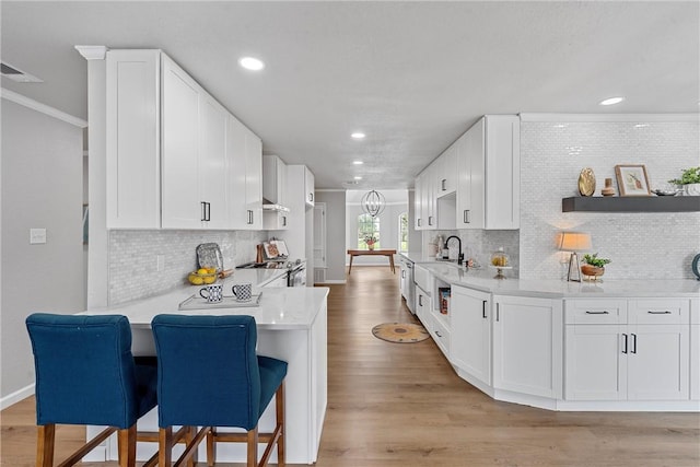 kitchen featuring white cabinets, tasteful backsplash, stainless steel range oven, kitchen peninsula, and a breakfast bar area