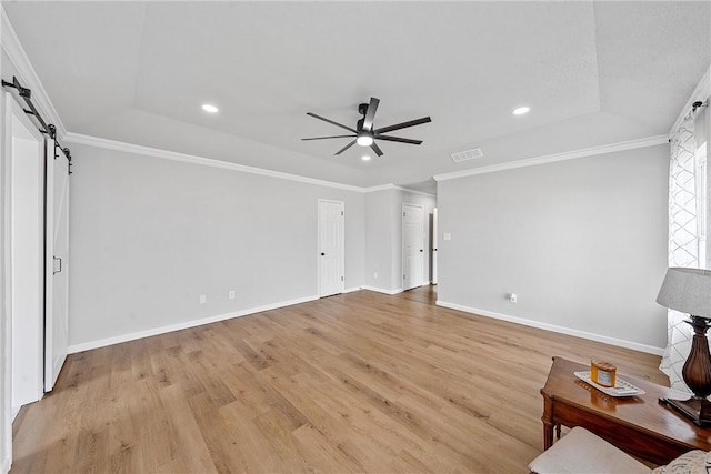 unfurnished living room featuring a barn door, light hardwood / wood-style floors, crown molding, and a tray ceiling