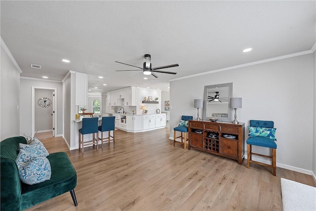 living room with sink, light hardwood / wood-style flooring, a textured ceiling, and ornamental molding