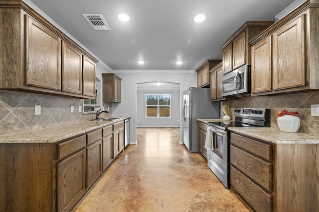 kitchen with sink, tasteful backsplash, light stone counters, crown molding, and appliances with stainless steel finishes