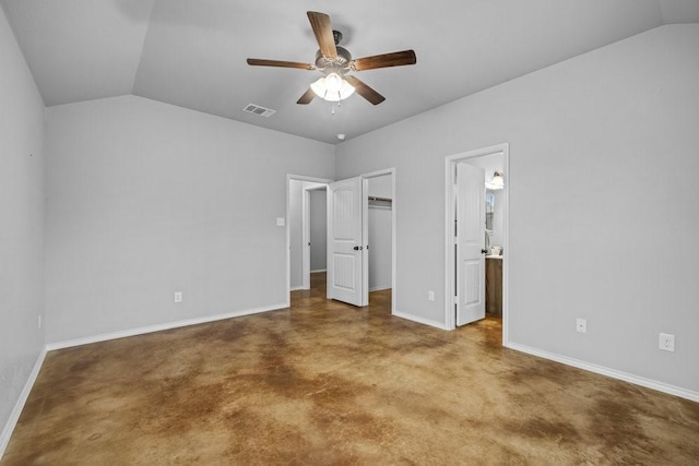 unfurnished bedroom with a walk in closet, ensuite bathroom, vaulted ceiling, ceiling fan, and concrete floors