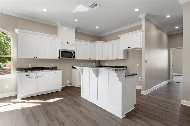 kitchen with a breakfast bar, dark hardwood / wood-style floors, ornamental molding, an island with sink, and white cabinetry