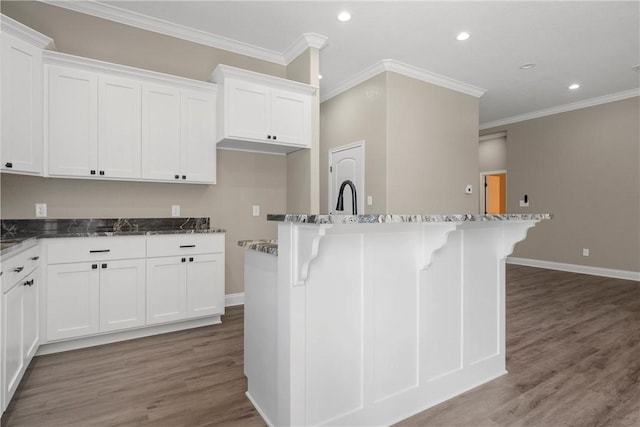 kitchen featuring crown molding, a center island with sink, hardwood / wood-style flooring, dark stone countertops, and white cabinetry