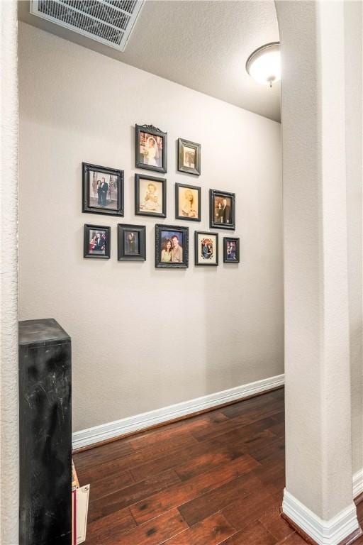 corridor with dark wood-type flooring, baseboards, and visible vents