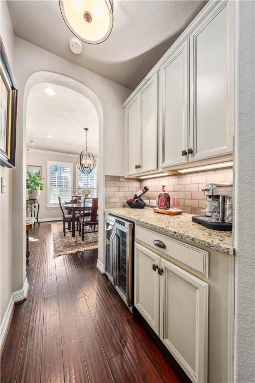 kitchen featuring dark wood-style floors, baseboards, arched walkways, decorative backsplash, and wine cooler