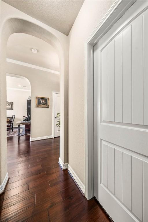 hallway featuring baseboards, arched walkways, and dark wood-style flooring