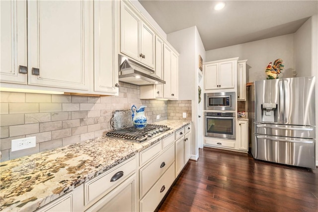 kitchen with light stone countertops, dark wood finished floors, under cabinet range hood, appliances with stainless steel finishes, and tasteful backsplash