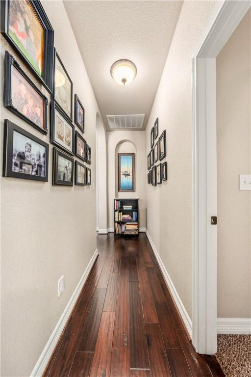 corridor with visible vents, baseboards, dark wood-type flooring, and arched walkways