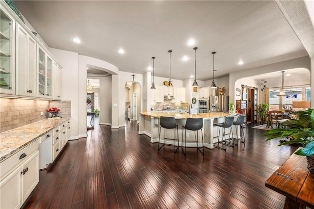 kitchen with light stone counters, dark wood-style floors, arched walkways, and stainless steel appliances