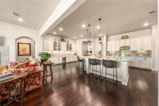 kitchen with under cabinet range hood, visible vents, white cabinetry, and a sink