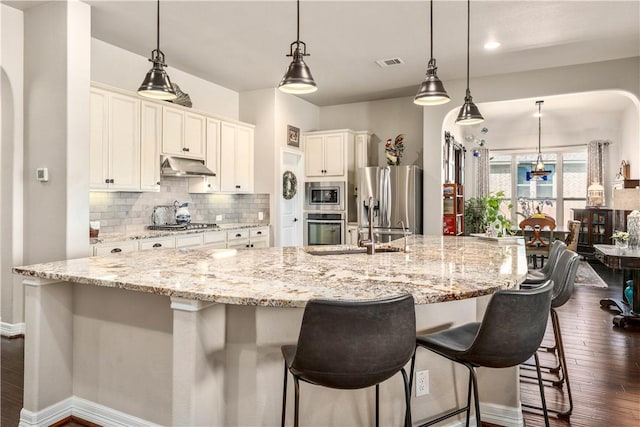 kitchen with visible vents, arched walkways, decorative backsplash, under cabinet range hood, and appliances with stainless steel finishes