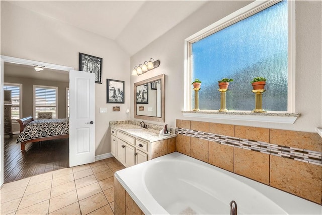 full bathroom with vanity, lofted ceiling, a relaxing tiled tub, tile patterned floors, and connected bathroom