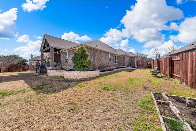 view of side of property with brick siding, a lawn, and a fenced backyard