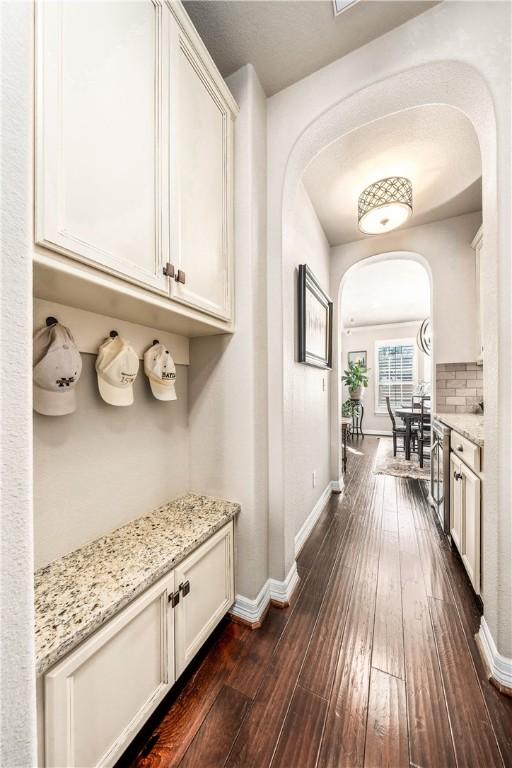 hallway with arched walkways, dark wood-type flooring, and baseboards