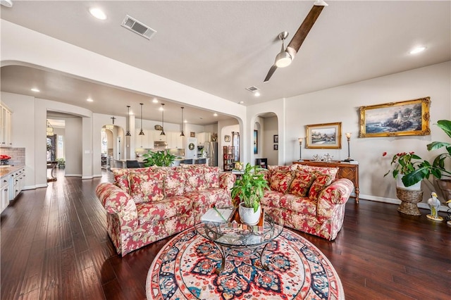 living area featuring visible vents, ceiling fan, baseboards, dark wood-style floors, and arched walkways