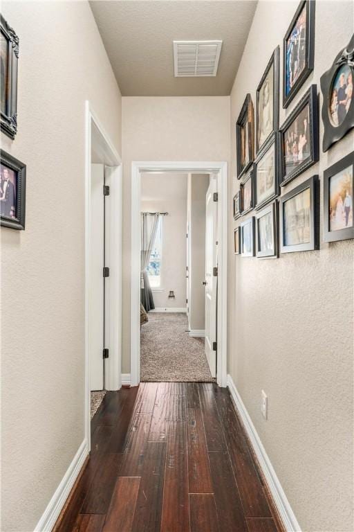 corridor with visible vents, baseboards, and dark wood-style flooring