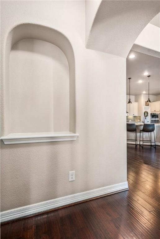 corridor featuring dark wood finished floors, arched walkways, and baseboards