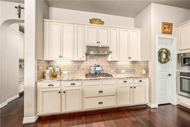 kitchen featuring under cabinet range hood, stainless steel appliances, light stone counters, and dark wood-style flooring