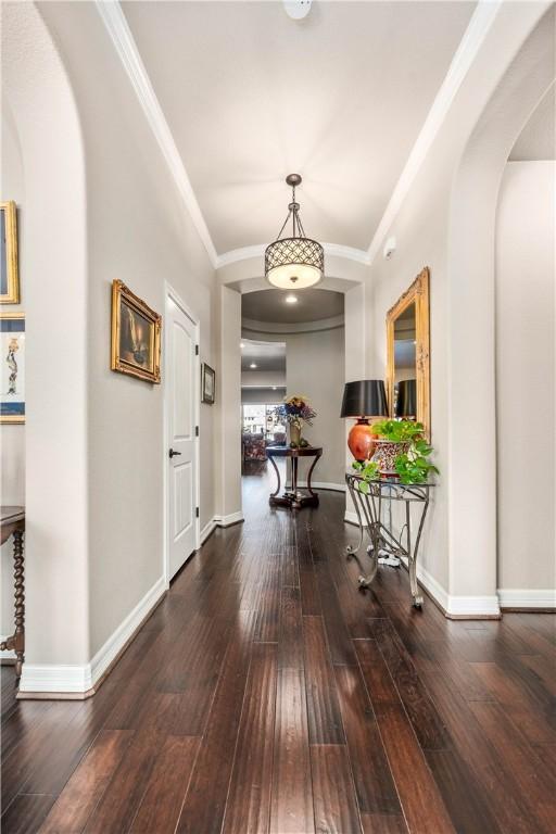 corridor featuring baseboards, arched walkways, wood-type flooring, and crown molding