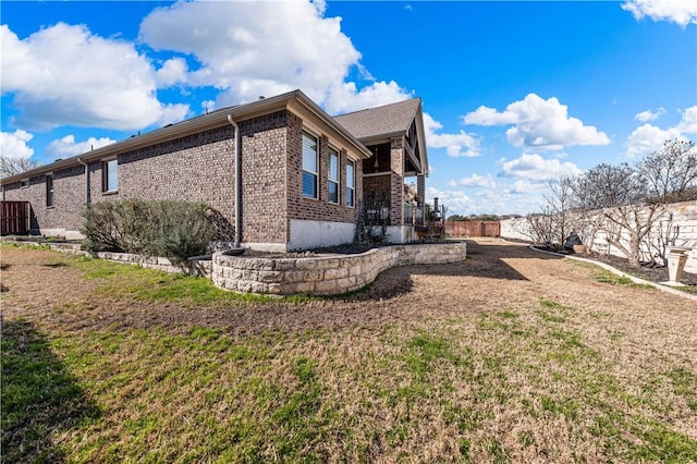 view of home's exterior with brick siding, a lawn, and fence