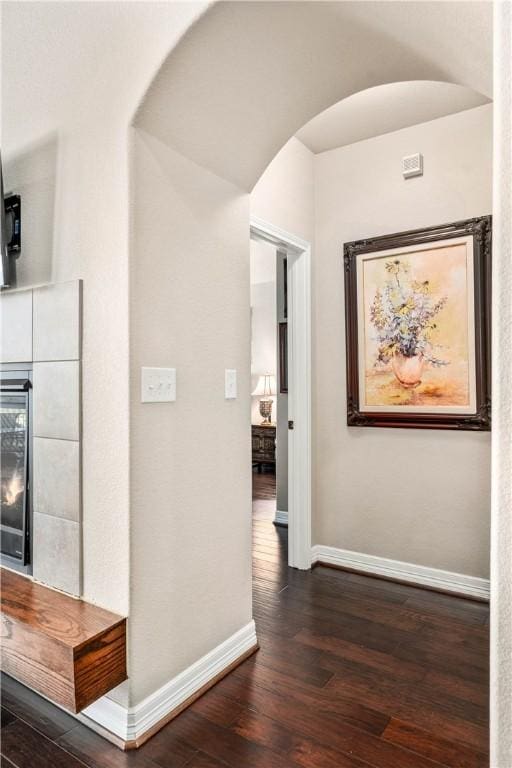 hallway with dark wood-style floors, wine cooler, arched walkways, and baseboards