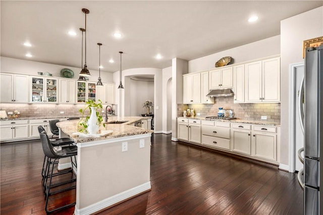 kitchen with a sink, under cabinet range hood, white cabinetry, stainless steel appliances, and arched walkways