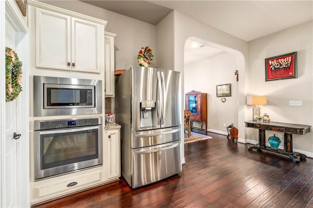 kitchen featuring stainless steel appliances, arched walkways, baseboards, and dark wood finished floors