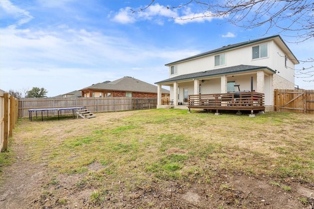 rear view of property featuring a trampoline, a fenced backyard, a yard, and a wooden deck