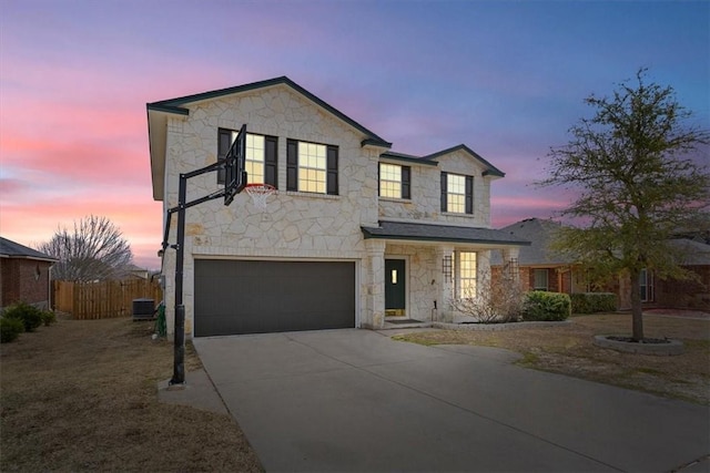 traditional-style house featuring central AC unit, concrete driveway, stone siding, an attached garage, and fence