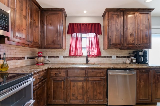 kitchen featuring tasteful backsplash, light stone countertops, appliances with stainless steel finishes, and sink