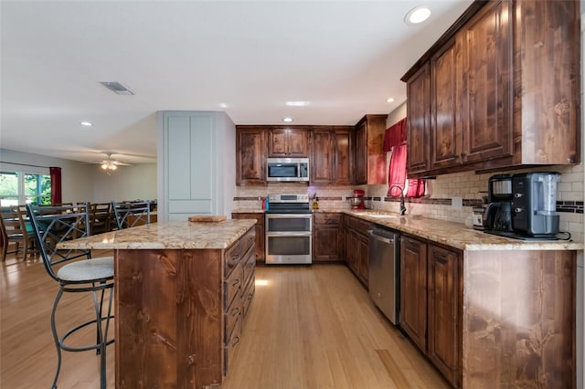 kitchen with appliances with stainless steel finishes, sink, light stone counters, and light wood-type flooring