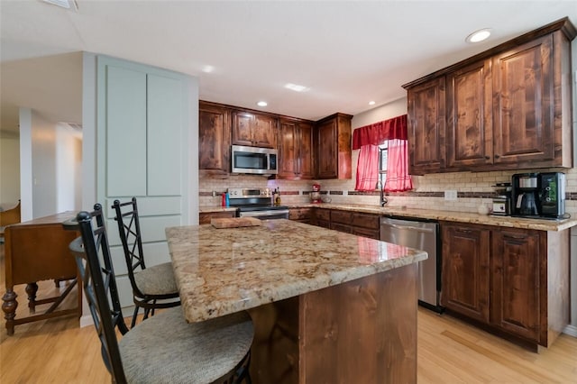 kitchen with light stone counters, stainless steel appliances, a center island, and light hardwood / wood-style floors