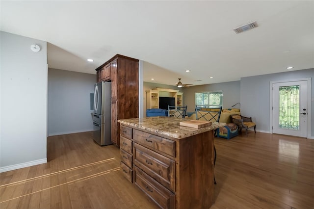 kitchen with dark hardwood / wood-style flooring, a kitchen bar, light stone counters, and stainless steel refrigerator