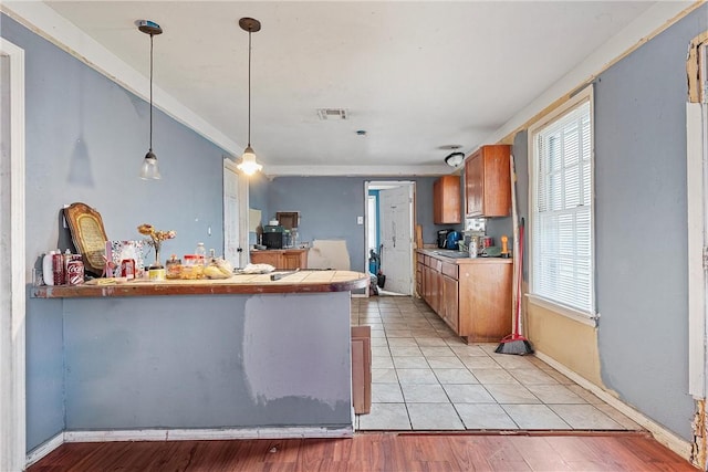 kitchen with visible vents, pendant lighting, brown cabinets, a peninsula, and light wood-style floors