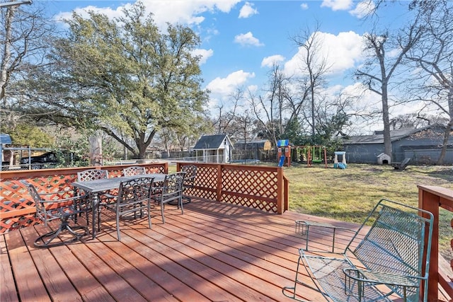 deck with a trampoline, outdoor dining area, a playground, a yard, and a fenced backyard