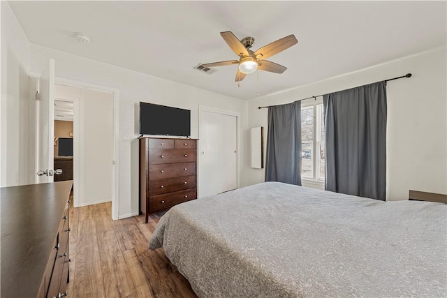 bedroom with ceiling fan, wood finished floors, visible vents, baseboards, and a closet