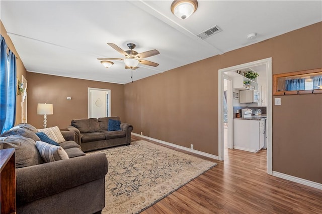 living room with a ceiling fan, visible vents, baseboards, and wood finished floors