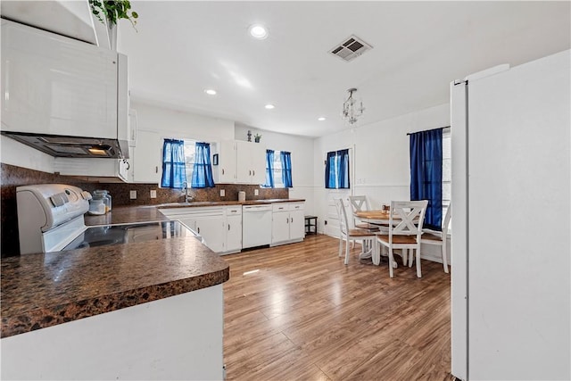 kitchen with dark countertops, visible vents, white cabinetry, a sink, and white appliances