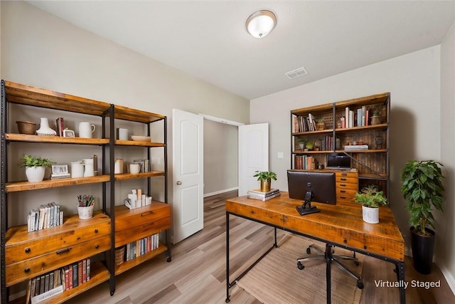 home office with light wood-style flooring and visible vents